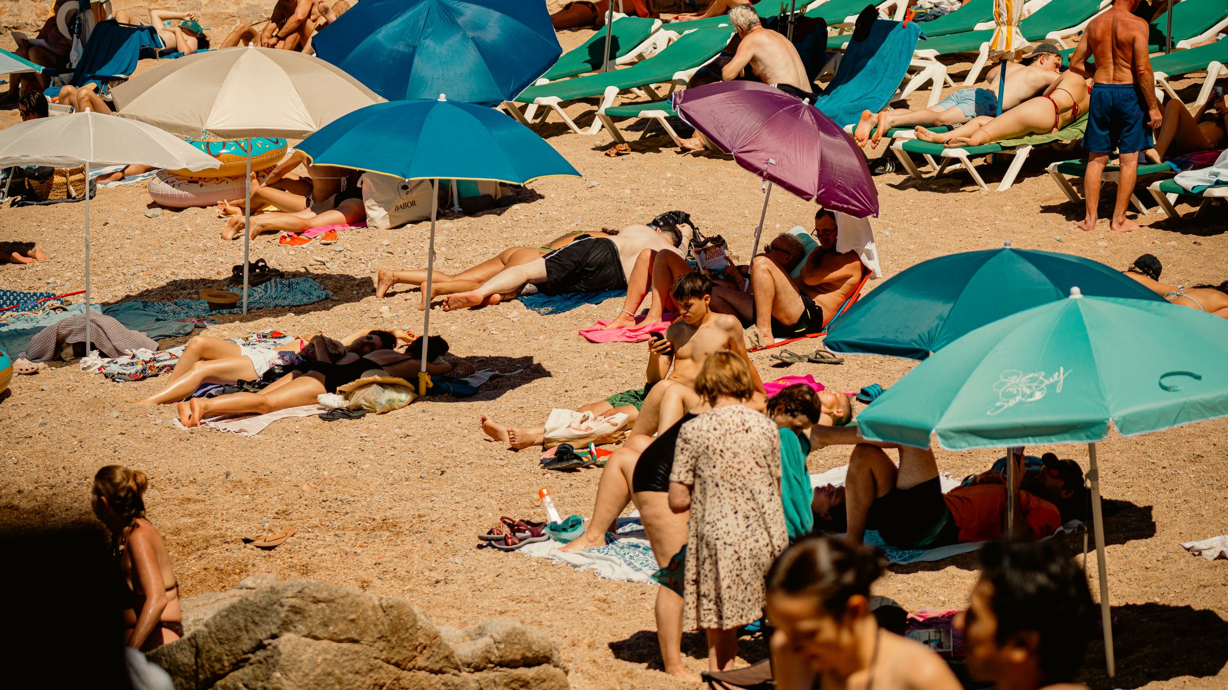 Summer beach packed wall to wall with coloured parasols and rows of loungers